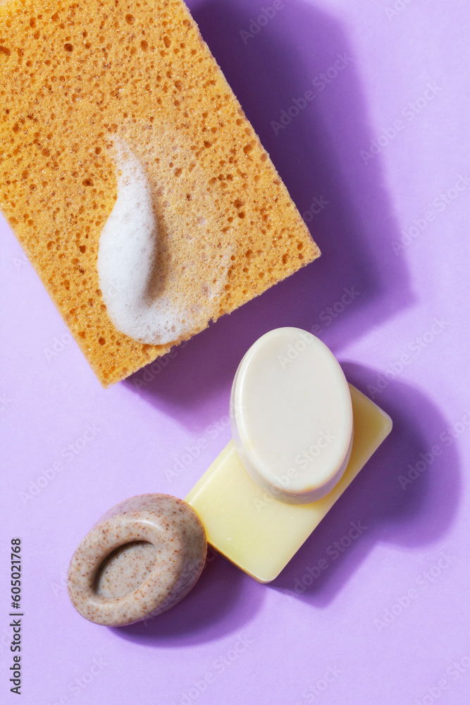 Handmade soap with the addition of coffee and wild herbs and a sponge with foam on a purple background.