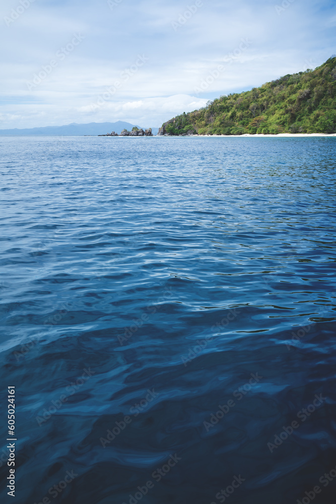 Deep blue ocean waves with lush green island and rocks in Palawan, Philippines