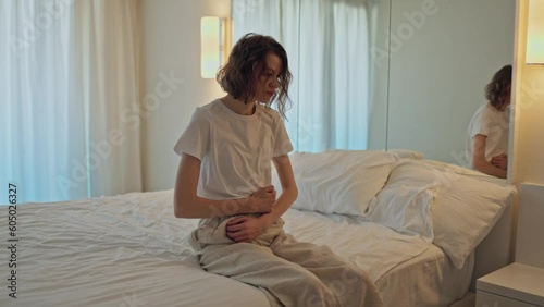 Woman is sitting on the bed. Experiencing pain in the abdomen