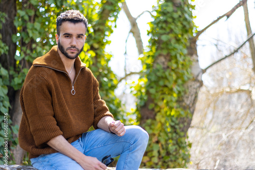 Portrait of attractive bearded young man sitting in a natural environment. Handsome young man sitting outside looking at camera