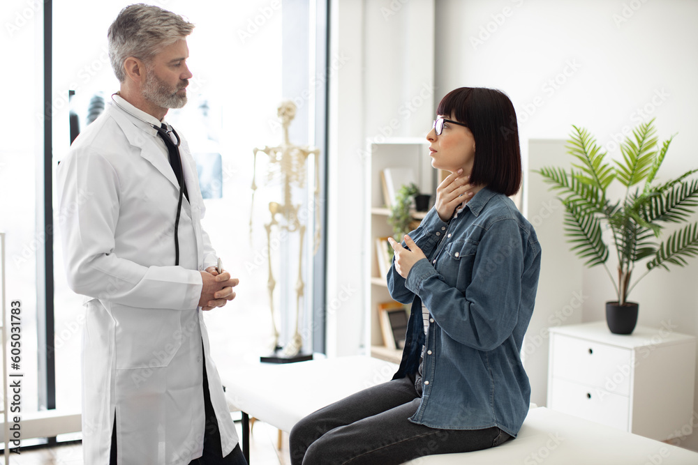 Obraz premium Attractive young woman holding hand on throat while describing health condition to bearded man in lab coat. Confident therapist giving consultation about illness to female patient at modern hospital.