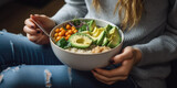 Woman in shirt and jeans eating vegan superbowl. Buddha bowl with hummus, vegetable, salad, beans, couscous and avocado.
