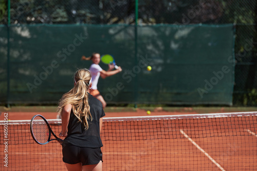 Young girls in a lively tennis match on a sunny day, demonstrating their skills and enthusiasm on a modern tennis court. © .shock