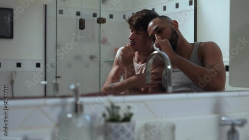 jovem casal gay inter racial brasileiro no banheiro escovando os dentes juntos sentados na banheira em frente ao espelho no dia dos namorados photo