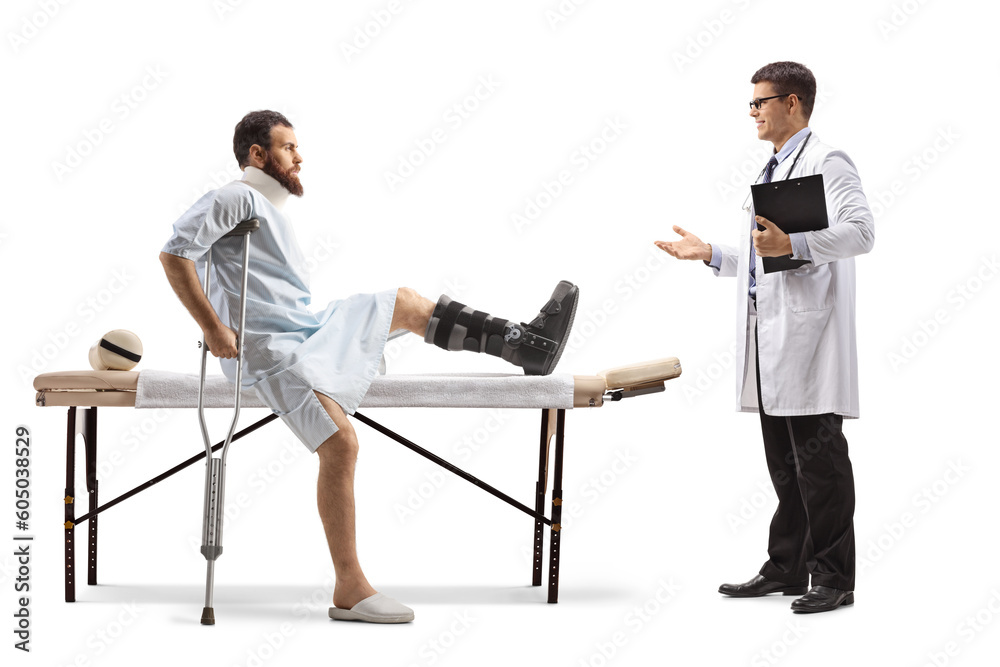 Fototapeta premium Injured man with an orthopedic boot and neck collar sitting on a therapy table and having conversation with a doctor