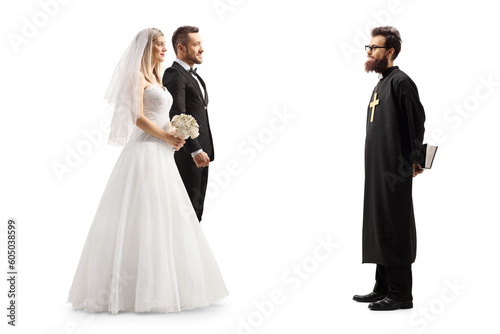 Full length profile shot of a priest and a bride and groom
