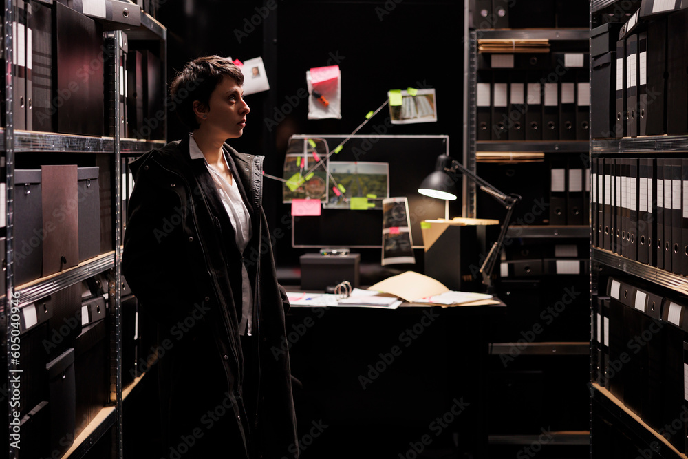 Fototapeta premium Private detective working late at night at confidential case, reviewing suspect report in arhive room. Investigator in formal suit discovery fraud evidence. Criminology department concept
