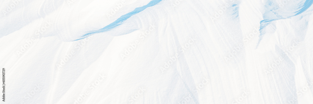 Obraz premium Wide panoramic winter background with snowy ground. Natural snow texture. Wind sculpted patterns on snow surface. Arctic, Polar region.