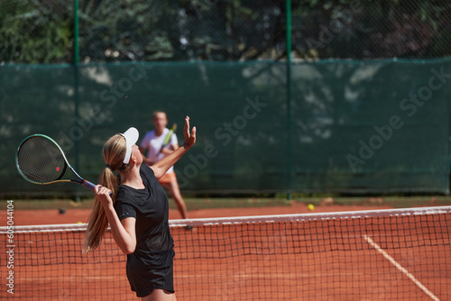 Young girls in a lively tennis match on a sunny day, demonstrating their skills and enthusiasm on a modern tennis court. © .shock