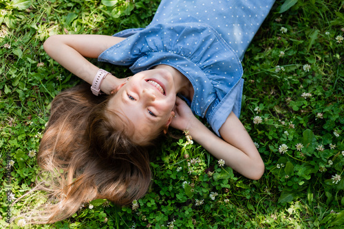 happy little girl lying on the green grass in summer top view