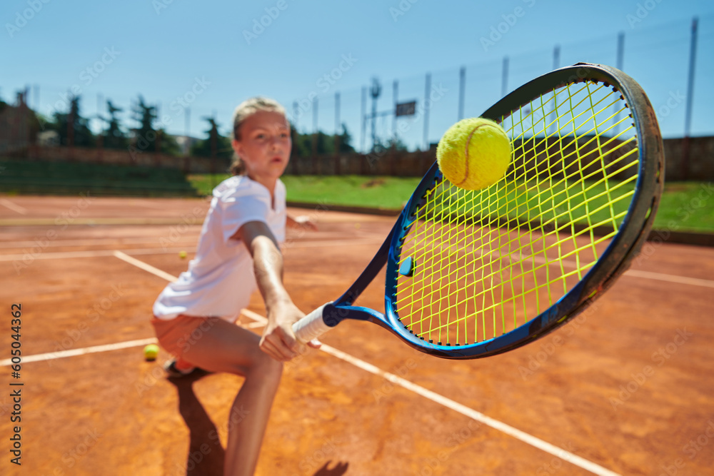 Close up photo of a young girl showing professional tennis skills in a competitive match on a sunny day, surrounded by the modern aesthetics of a tennis court.