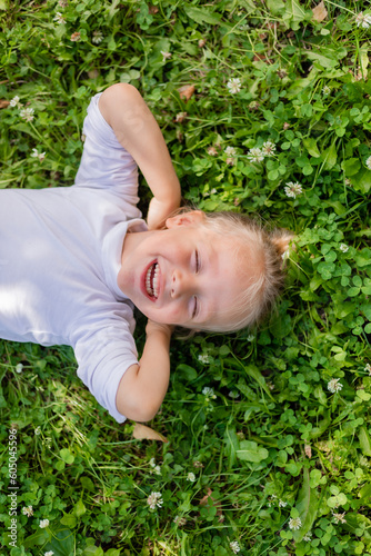 happy little boy lying on the green grass in summer top view in a white turtleneck, space for text