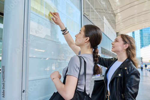 Fotografi Two young females reading the transport timetable on the scoreboard