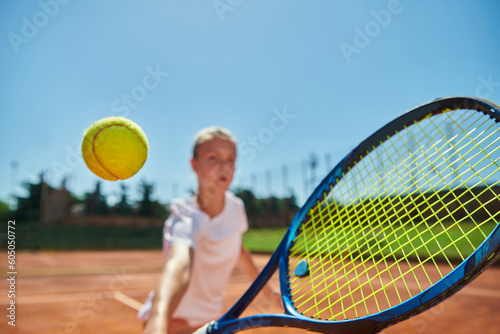 Close up photo of a young girl showing professional tennis skills in a competitive match on a sunny day, surrounded by the modern aesthetics of a tennis court. © .shock