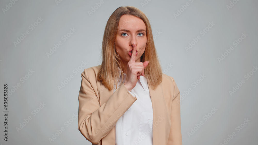 Shh be quiet please, keep my secret. Portrait of young businesswoman presses index finger to lips makes silence gesture sign do not tell anything. Female girl in suit. Pretty woman on gray background Shh be quiet please, keep my secret. Portrait of young businesswoman presses index finger to lips makes silence gesture sign do not tell anything. Female girl in suit. Pretty woman on gray background