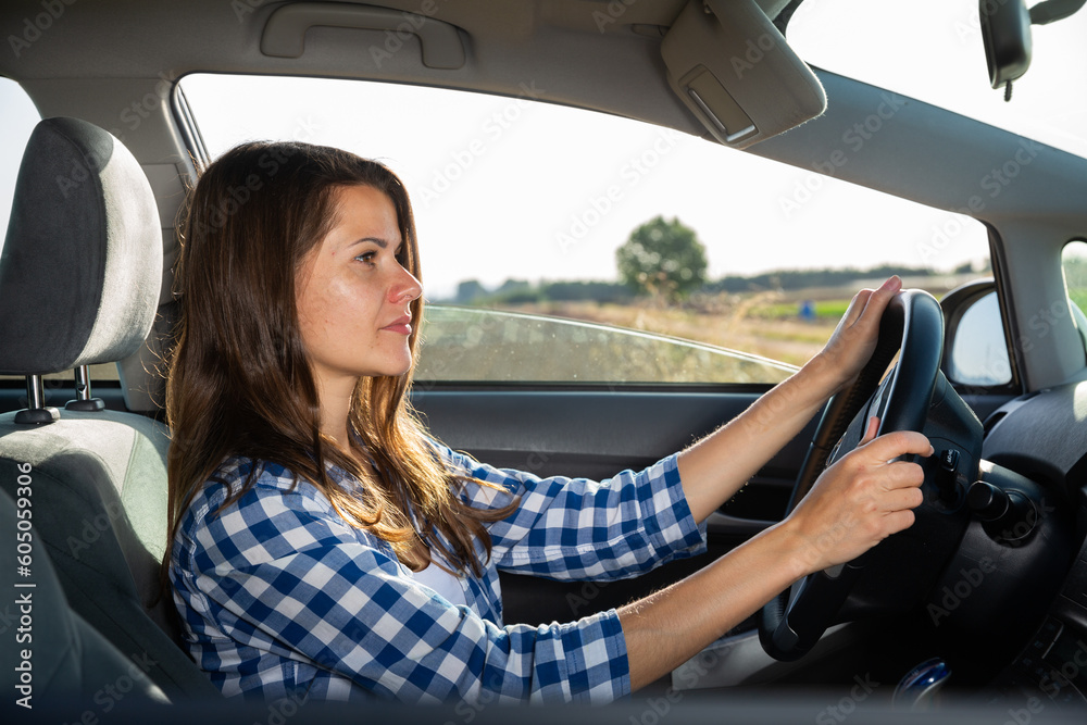 Positive young adult woman driving car during solo trip, side view