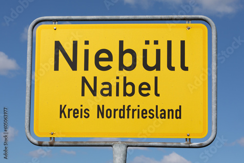 Zweisprachiges Ortsschild (deutsch und nordfriesisch) von Niebüll bzw. Naibel in Nordfriesland, Schleswig-Holstein, Deutschland, mit blauem Himmel und Wolken.