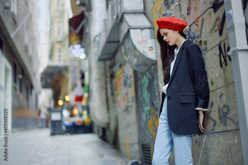 Fashion woman portrait walking tourist in stylish clothes with red lips walking down a narrow city street, travel, cinematic color, retro vintage style, dramatic against a wall with graffiti.