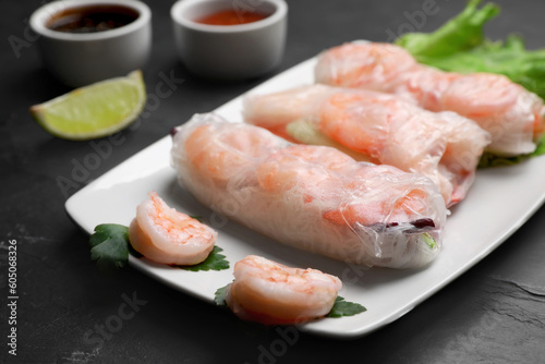Delicious spring rolls with shrimps wrapped in rice paper served on black table, closeup