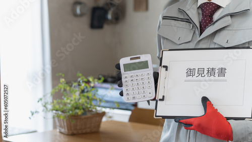 リビング・キッチンで電卓と見積書を持つ作業服の男性