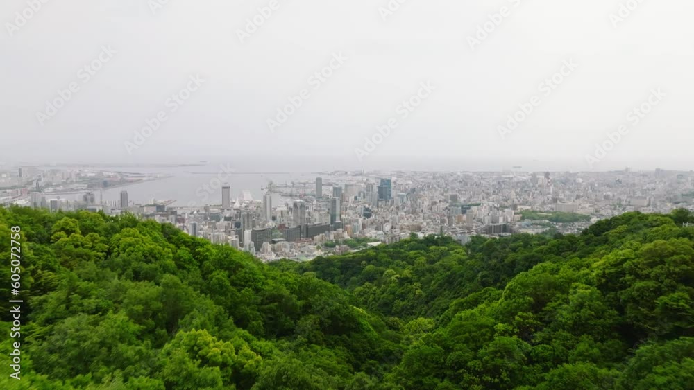 Flying over forested mountains to modern buildings in downtown Kobe City