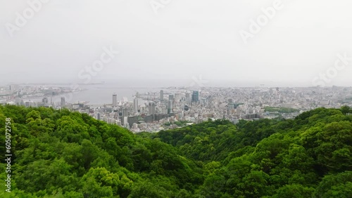 Flying over forested mountains to modern buildings in downtown Kobe City