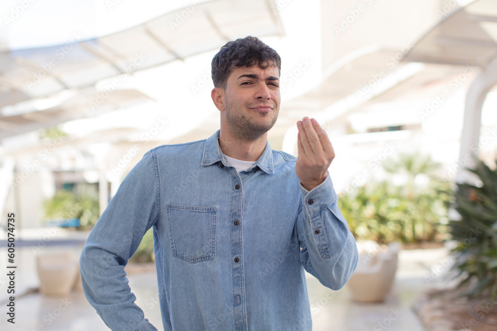 Naklejka premium young handsome man making capice or money gesture, telling you to pay your debts!