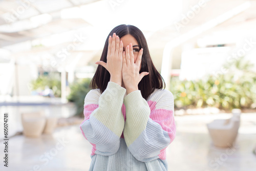 young pretty woman covering face with hands, peeking between fingers with surprised expression and looking to the side