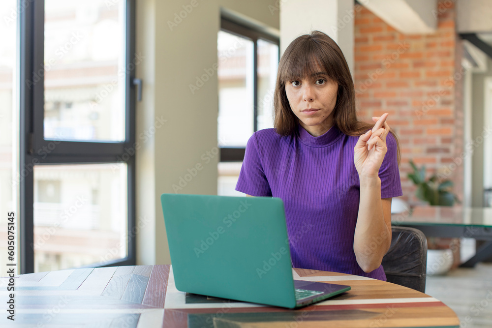 young pretty woman crossing fingers and hoping for good luck. desk laptop concept young pretty woman crossing fingers and hoping for good luck. desk laptop concept