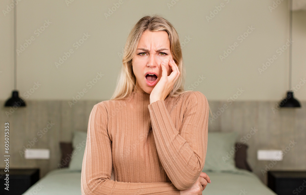 young pretty woman open-mouthed in shock and disbelief, with hand on cheek and arm crossed, feeling stupefied and amazed. bed concept young pretty woman open-mouthed in shock and disbelief, with hand on cheek and arm crossed, feeling stupefied and amazed. bed concept
