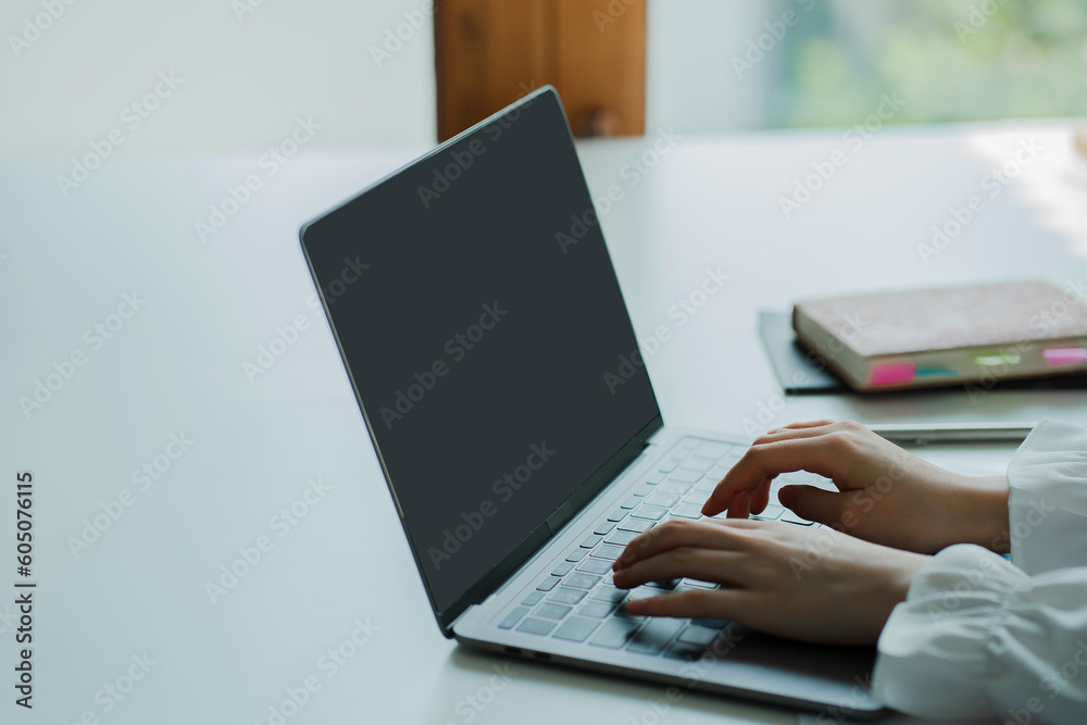 Fototapeta premium Young woman online job hunting working with laptop computer, blank screen at desk and close up working with computer hands.