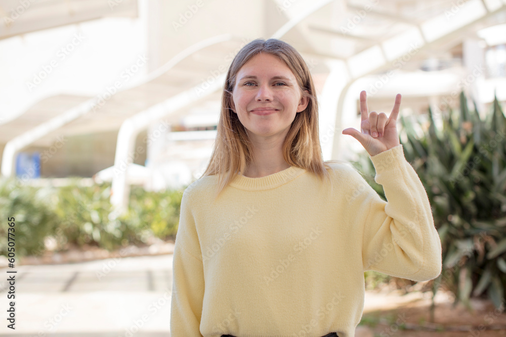 pretty young woman feeling happy, fun, confident, positive and rebellious, making rock or heavy metal sign with hand