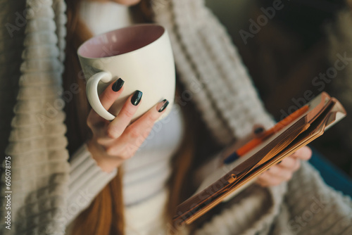 Close-up view of a woman's hand holding a cup and a notebook in which she writes down her thoughts. Relaxation lifestyle concept. Close-up, indoors. People