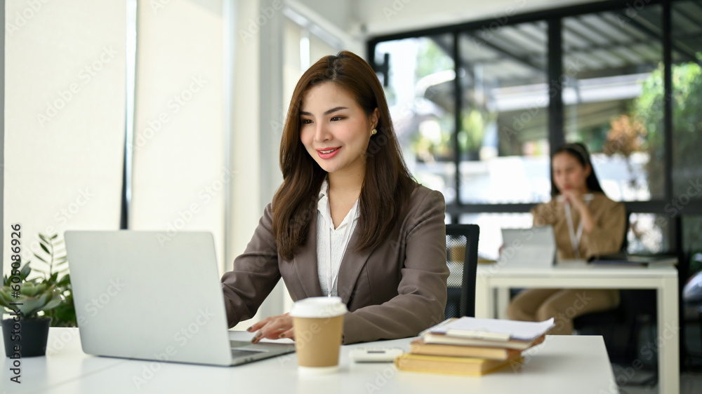 Smiling Asian businesswoman working on her assignment on her laptop at her desk. Smiling Asian businesswoman working on her assignment on her laptop at her desk.