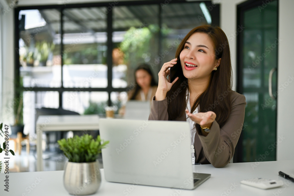 Charming Asian businesswoman talking on the phone with her client in the office. Charming Asian businesswoman talking on the phone with her client in the office.