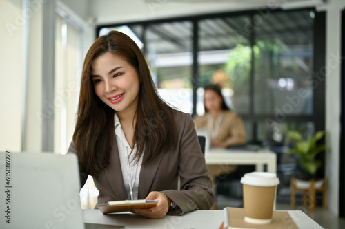 Smiling Asian businesswoman working on her tasks on laptop at her desk