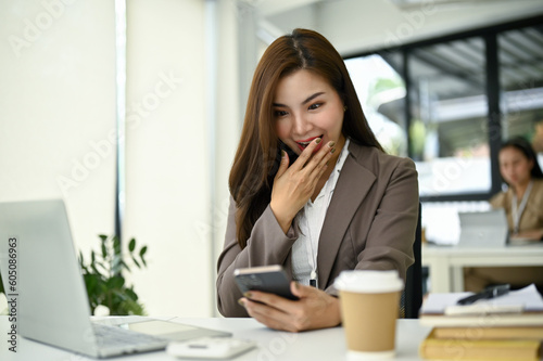 Excited and surprised Asian businesswoman receiving an unexpected message on her phone