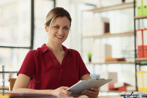 Happy female employee holds clipboard sitting at table