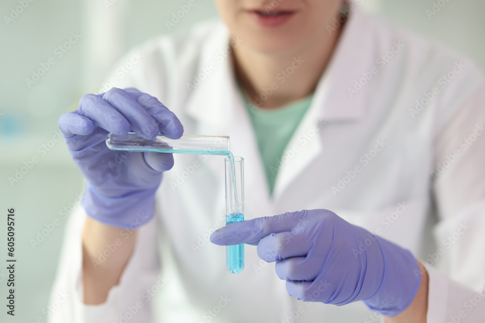Female laboratory assistant pours blue liquid from test tube