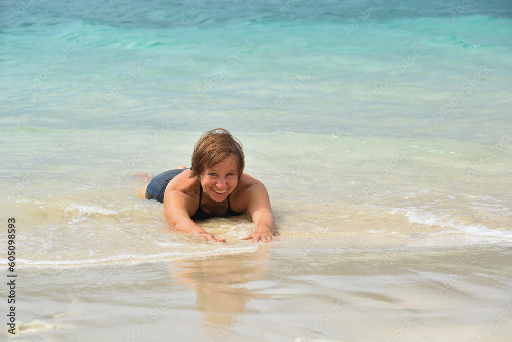 Happy attractive mature woman 50-60 lies in the water on the beach. Senior woman wear black swimsuit. Concept - travel, retirement, active elderly people, Philippines Happy attractive mature woman 50-60 lies in the water on the beach. Senior woman wear black swimsuit. Concept - travel, retirement, active elderly people, Philippines