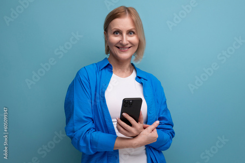 smiling middle aged woman mastering the technique of modernity and holding a smartphone with a mockup on a blue background copy space