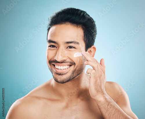 Skincare, beauty and man with face cream in a studio for a natural, wellness and health routine. Happy male model with facial spf, lotion or moisturizer for dermatology treatment by a blue background