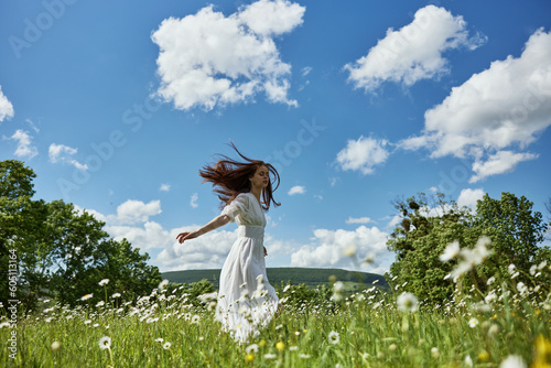 a happy woman in a light dress runs through a chamomile field against a clear sky