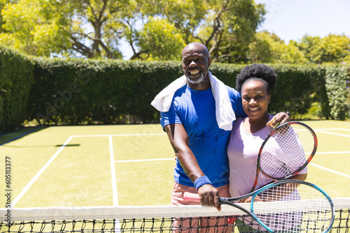 Portrait of happy senior african american couple with tennis rackets embracing on sunny grass court © wavebreak3