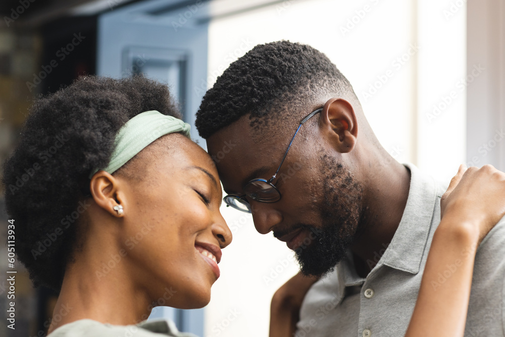 Happy, romantic african american couple touching heads embracing in kitchen