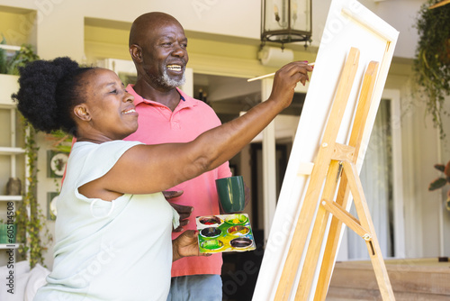 Happy senior african american couple painting canvas on easel together at home