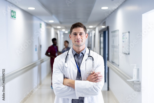 Unaltered portrait of caucasian male doctor with arms crossed  smiling in hospital corridor