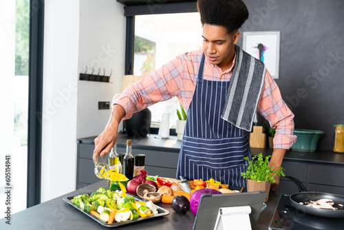 Happy biracial man wearing apron cooking dinner, pouring vegetables in kitchen, unaltered