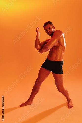Man bodybuilder boxer muscle workout with naked torso with abs posing in studio. Advertising, sports, active lifestyle, colored yellow light, competition, challenge concept. 