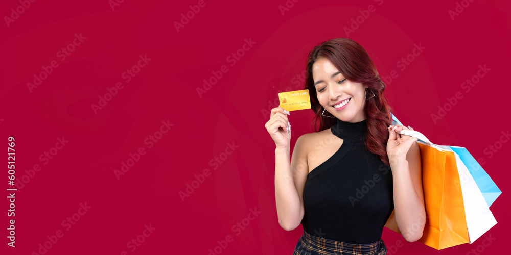 Banner: Stylish Asian woman in black dress holding shopping bags holding gold credit cards on crimson background. Beautiful Thai woman holding shopping bags holding gold credit cards on red background Banner: Stylish Asian woman in black dress holding shopping bags holding gold credit cards on crimson background. Beautiful Thai woman holding shopping bags holding gold credit cards on red background